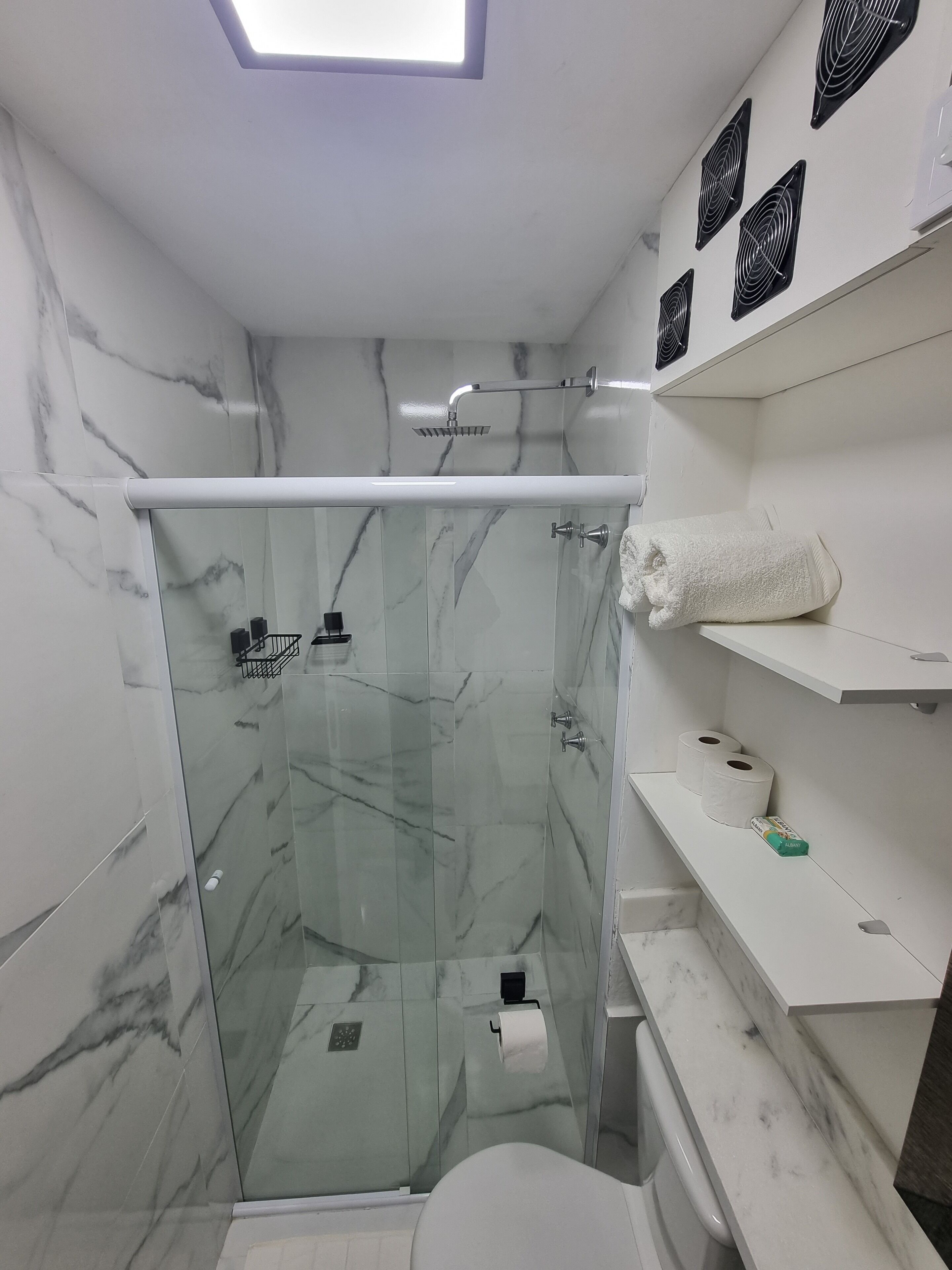 Un baño moderno con ducha envuelta en vidrio, paredes de mármol y accesorios blancos.