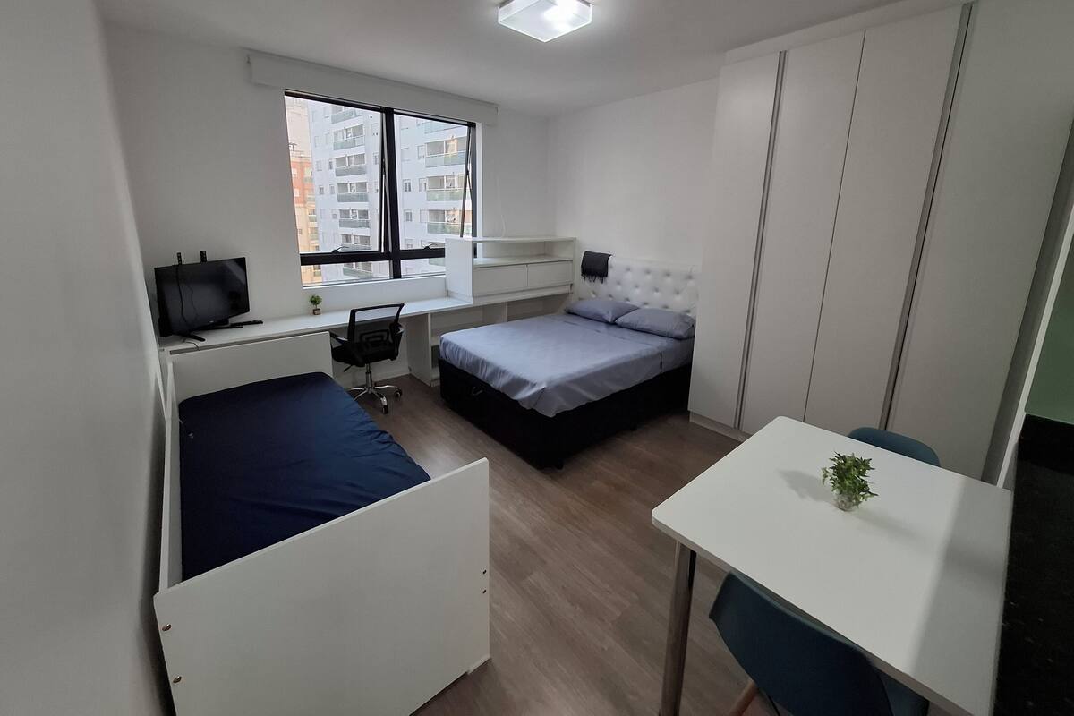 Une chambre à coucher de taille réduite, comprenant un lit, un bureau, une chaise et un téléviseur.
