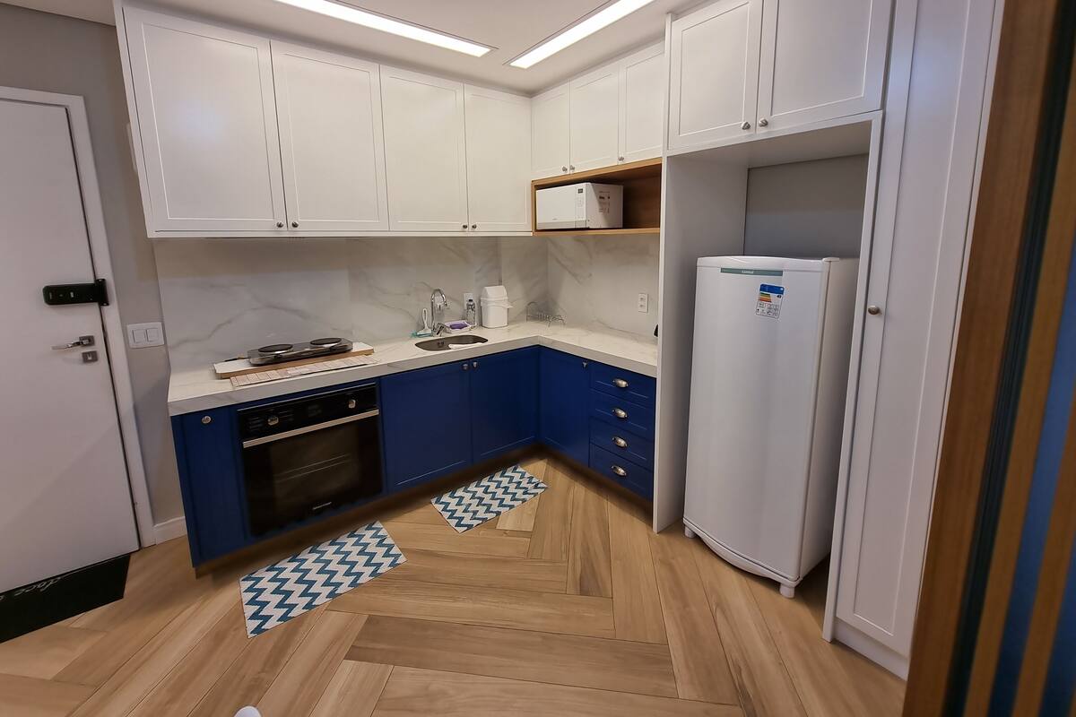 Une cuisine compacte avec des meubles blancs, un four encastré, un réfrigérateur et un four à micro-ondes.