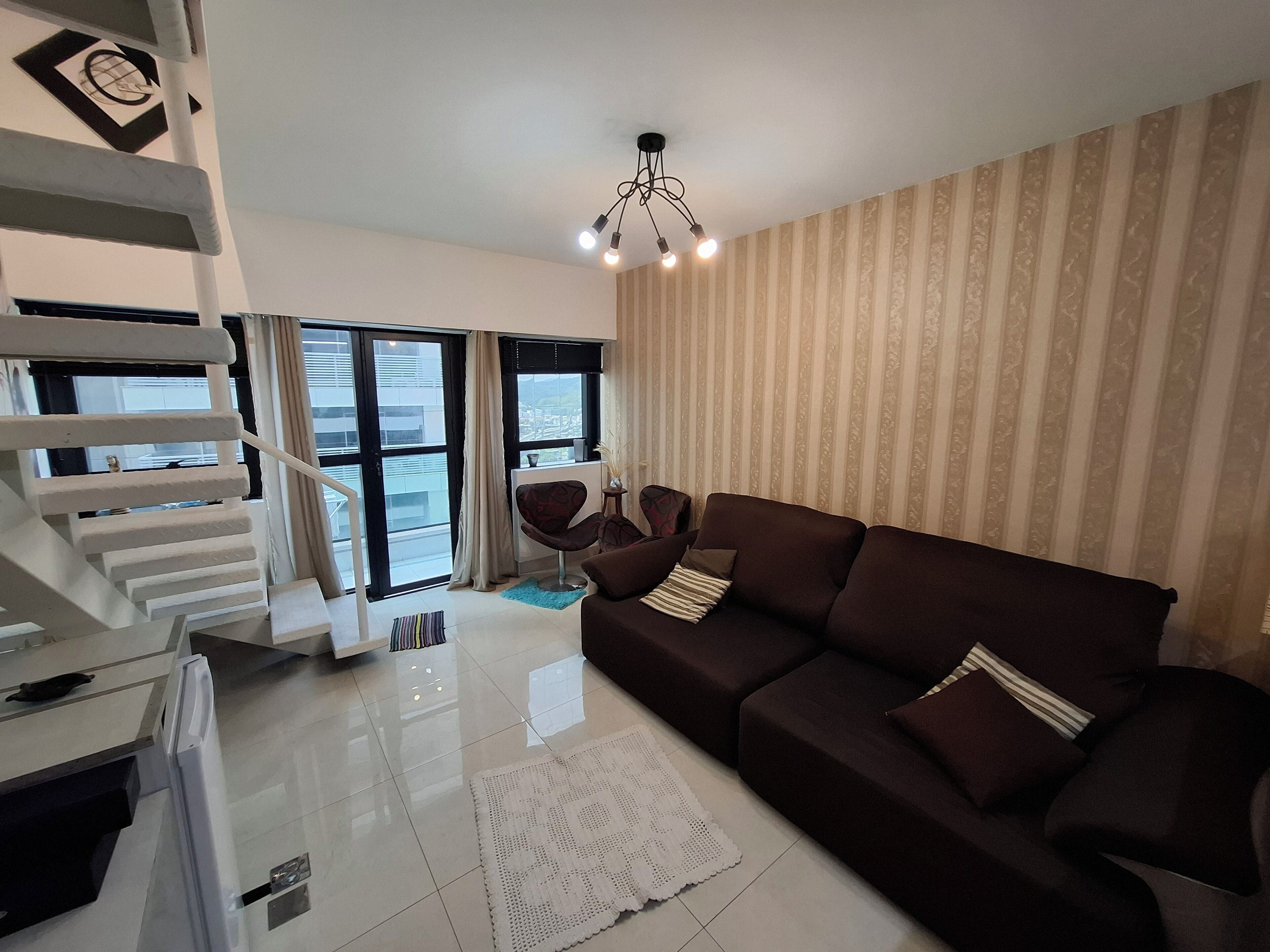 A modern living room with a dark brown sofa, a white coffee table, and a staircase with a white railing.