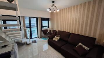 A modern living room with a dark brown sofa, a white coffee table, and a staircase with a white railing.