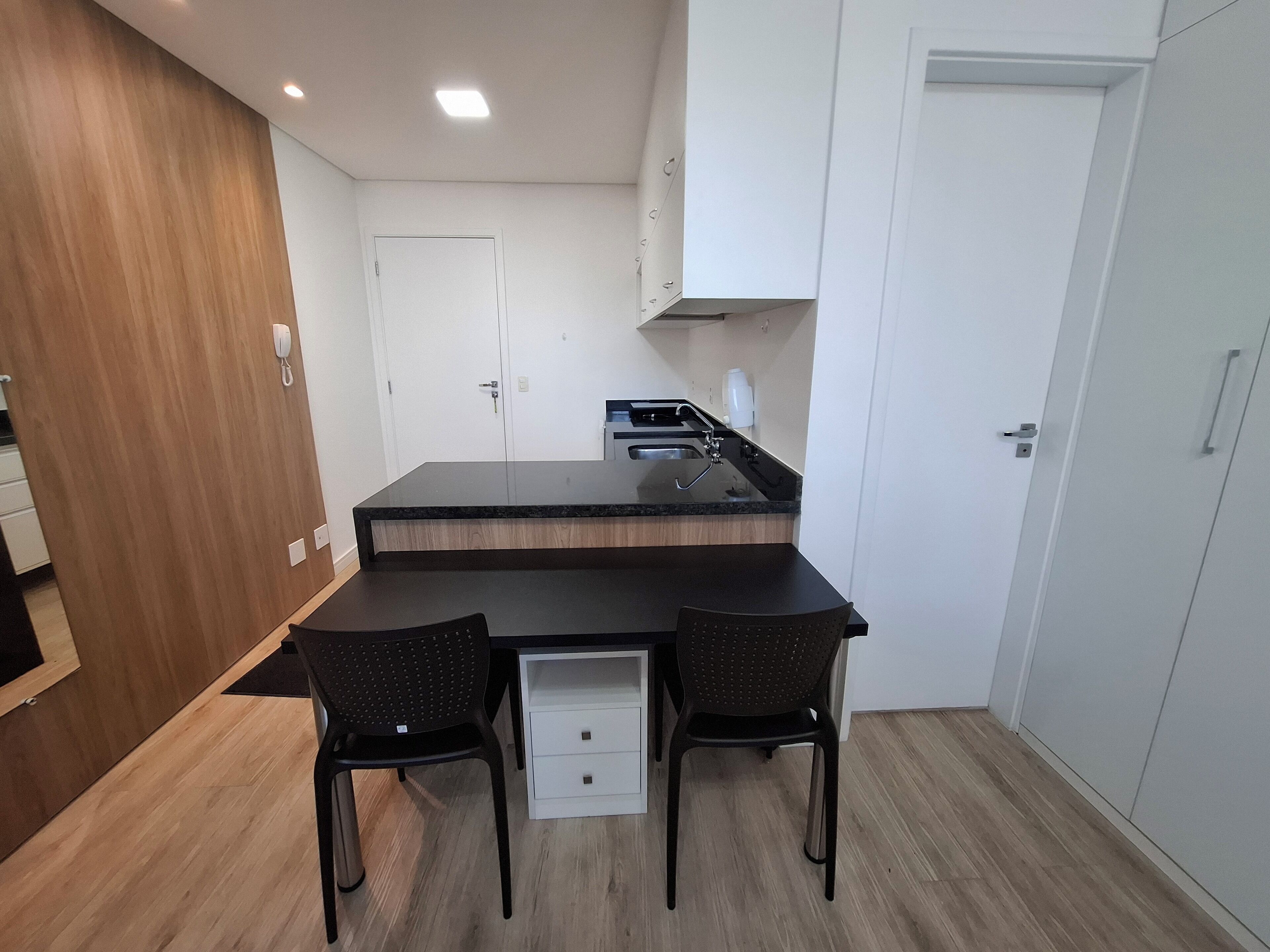 Una cocina compacta con una isla central, dos sillas, un armario blanco y una pared de madera.