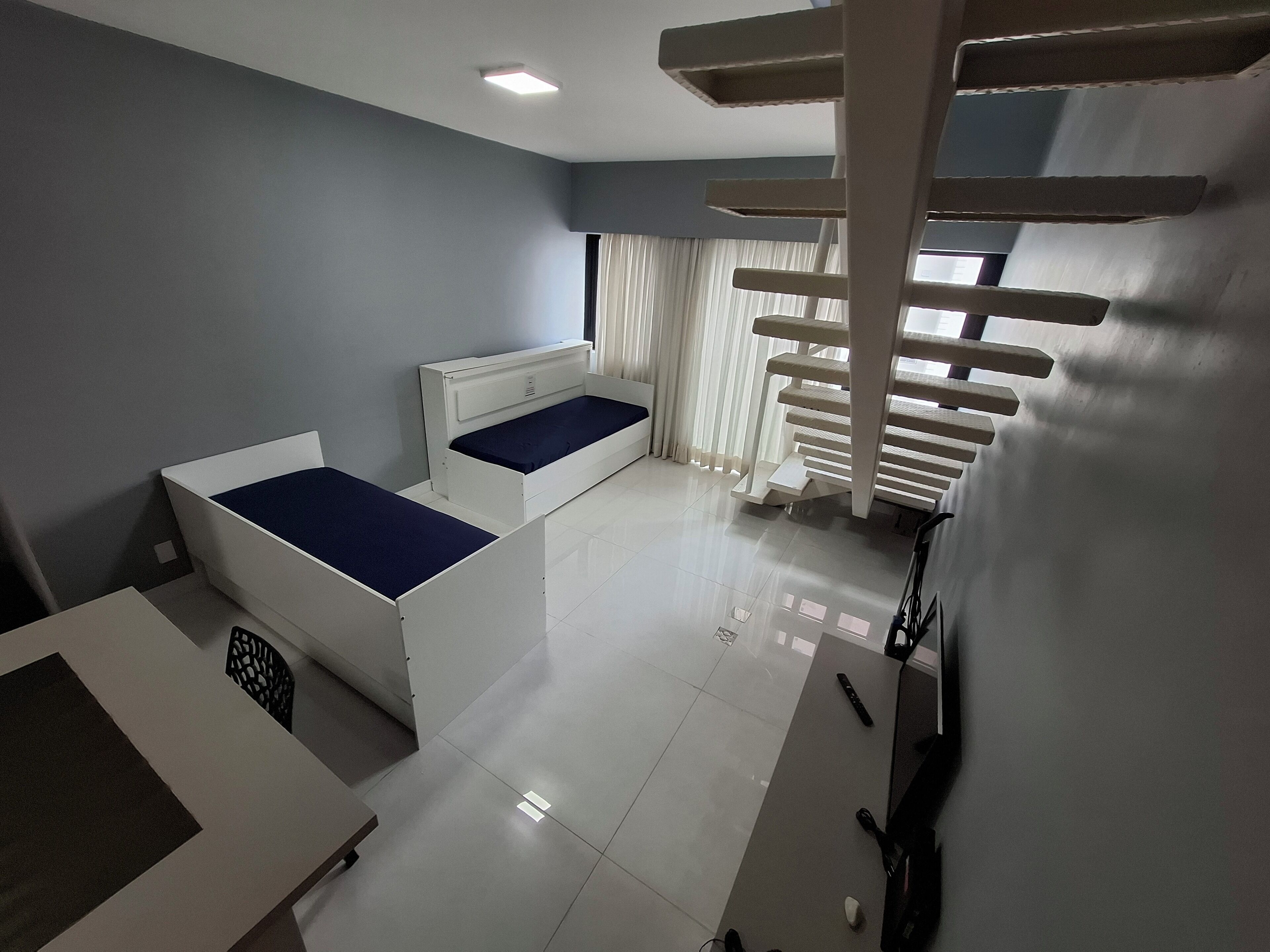 Quarto moderno com duas camas, uma escrivaninha e um arranhador para gatos.