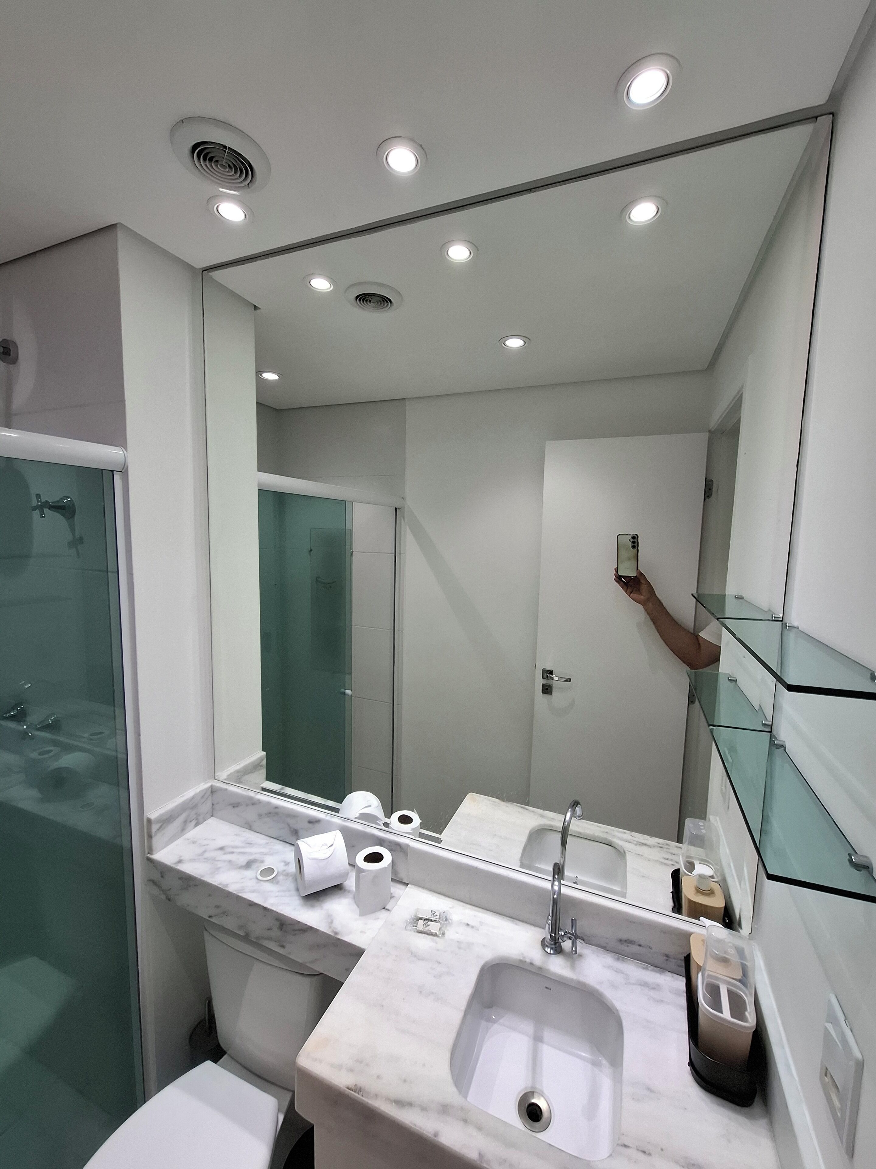 A modern bathroom with a glass shower enclosure, a marble sink, and a large mirror.