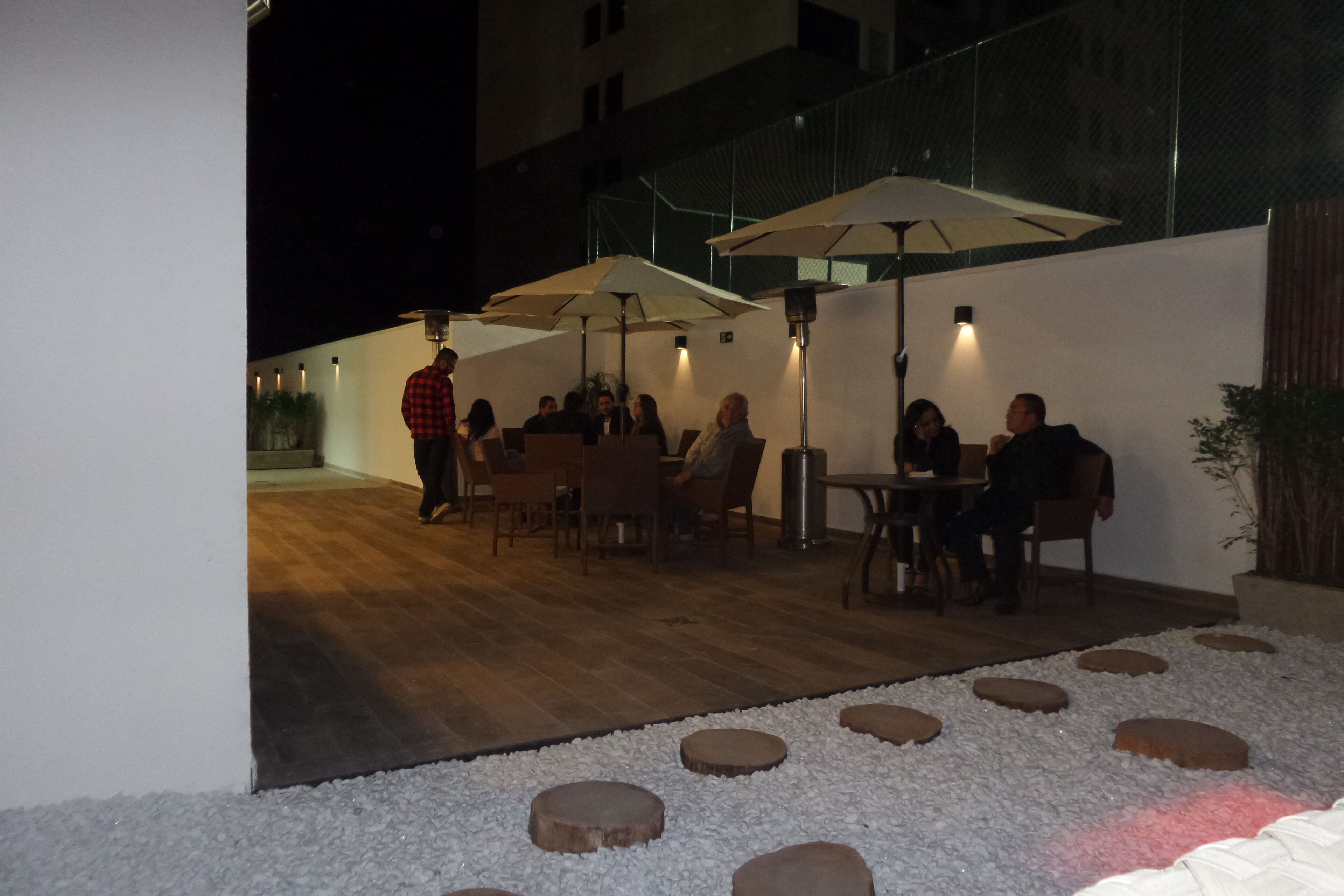 An outdoor patio area with wooden flooring, round stone planters, and tables with umbrellas.