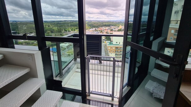 A high-rise building with a large glass window, a metal railing, and a view of a cityscape. - Edificio Selenita Loft e Duplex (Barueri)