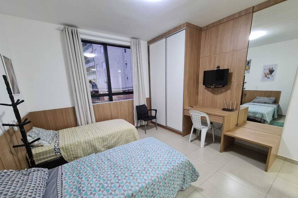 Une chambre avec deux lits, un bureau, une chaise, une télévision et une armoire.