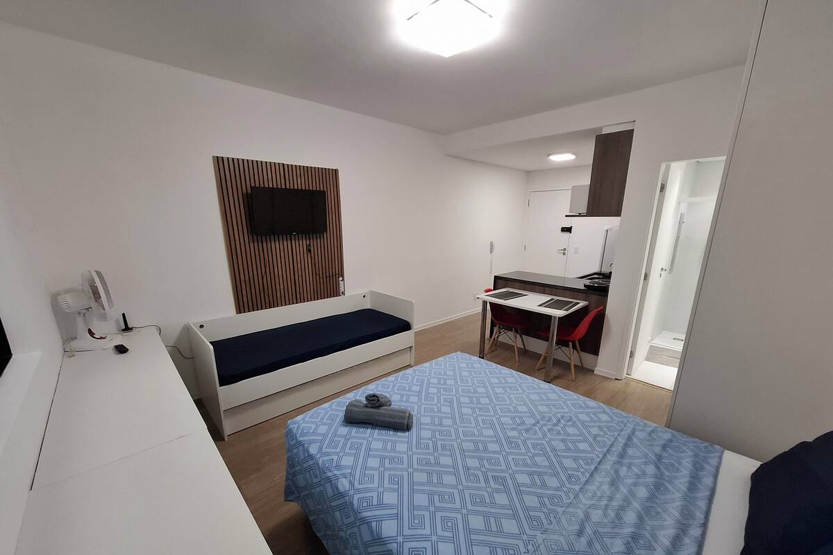 Une petite chambre comprenant un lit, un bureau et une kitchenette.