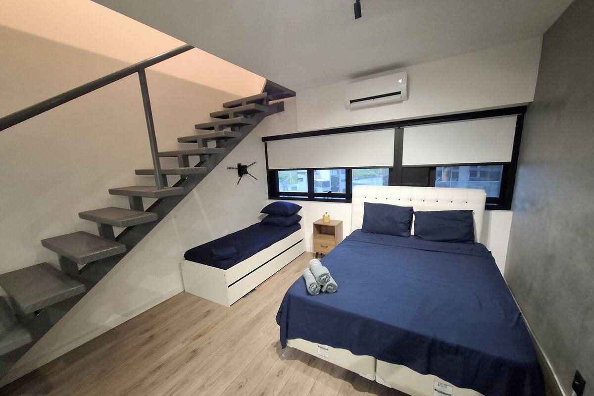 Une chambre moderne avec un lit intégré, une petite table de chevet, une commode, une fenêtre et un escalier.
