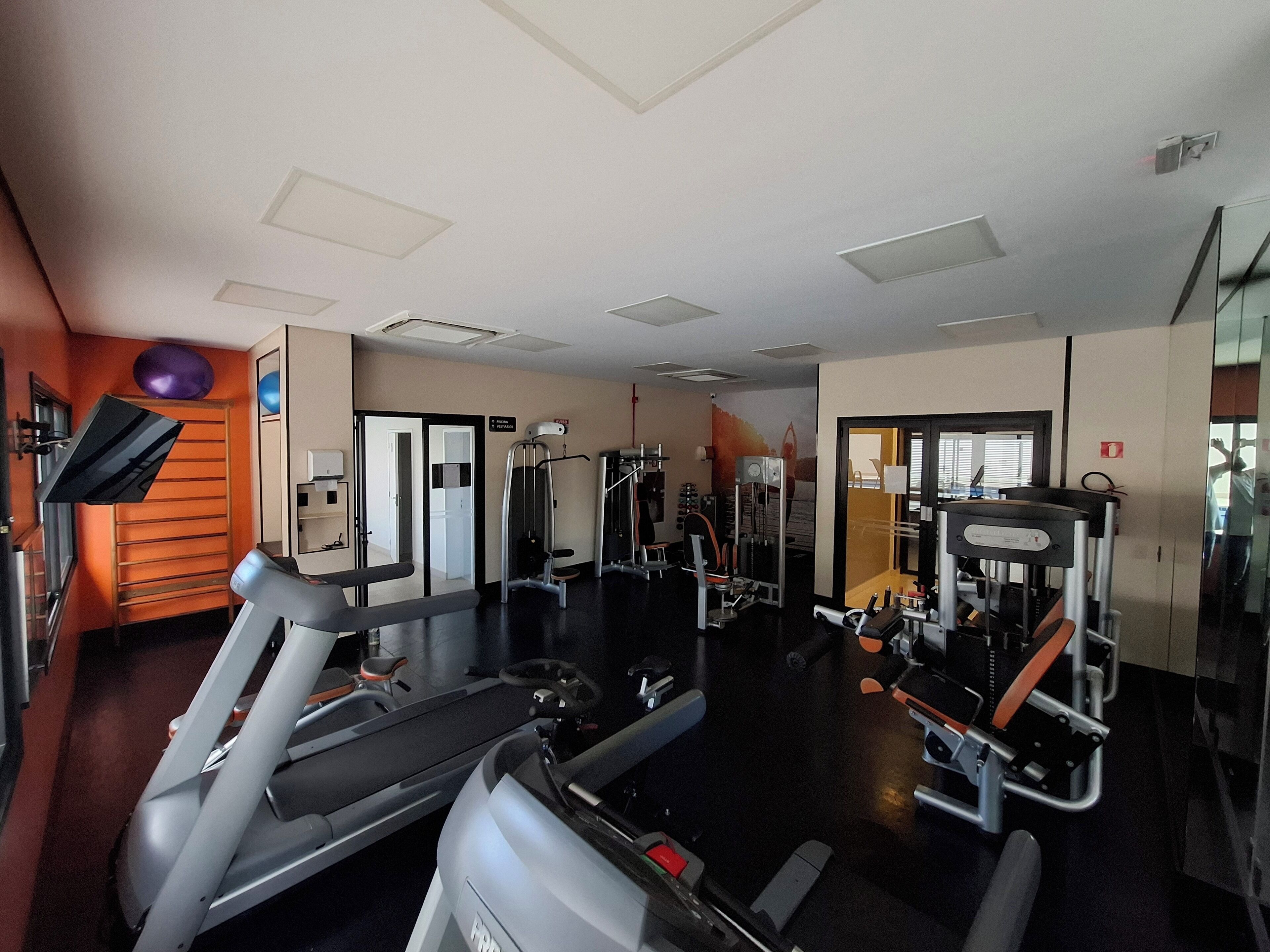 Un gimnasio con cintas de correr, máquinas de pesas y un espejo grande.