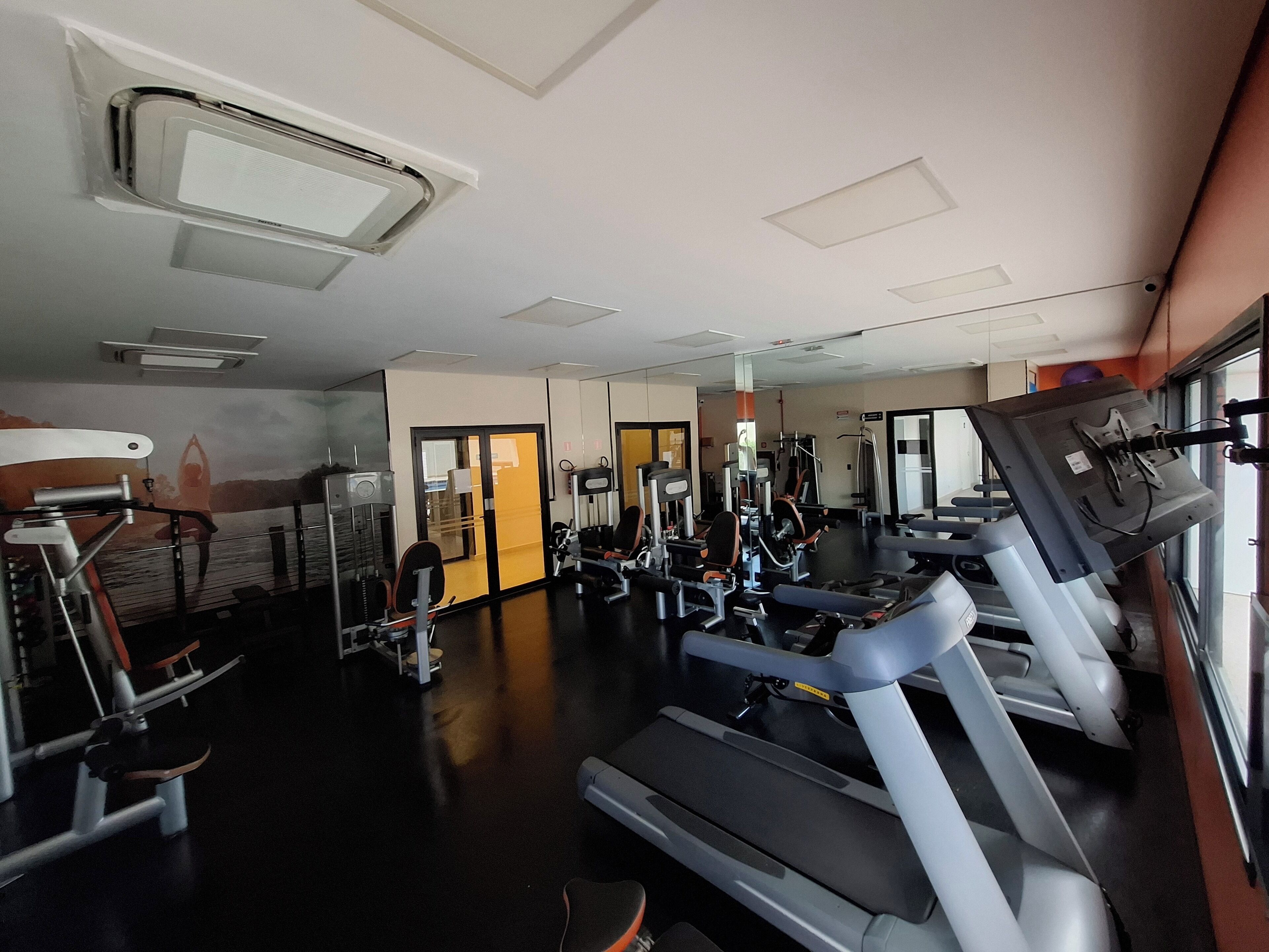 Ein Fitnessstudio mit Laufbändern, Kraftgeräten und einer Spiegelwand.