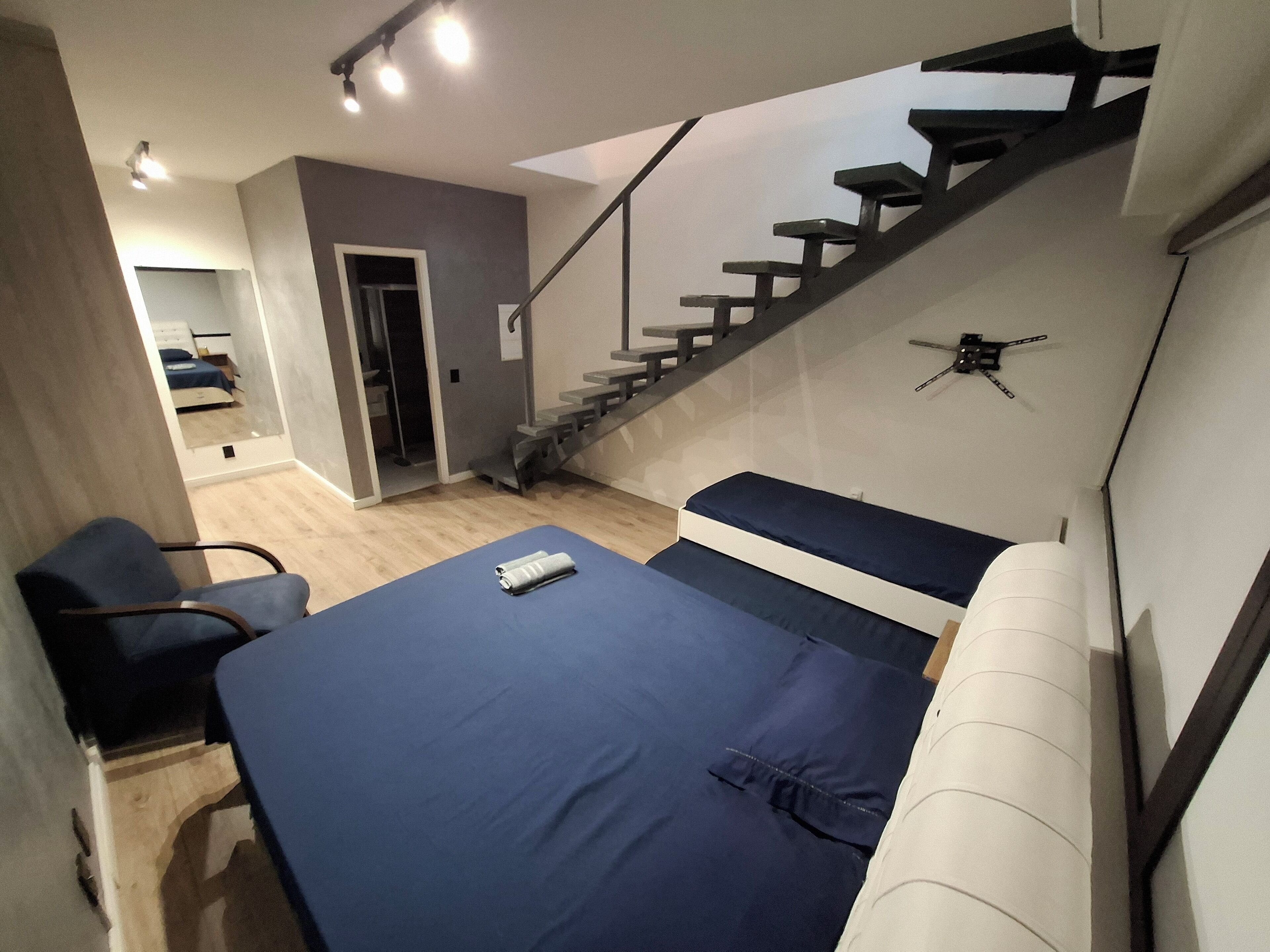 A modern room with a bed, a chair, a staircase, and a door leading to another room.