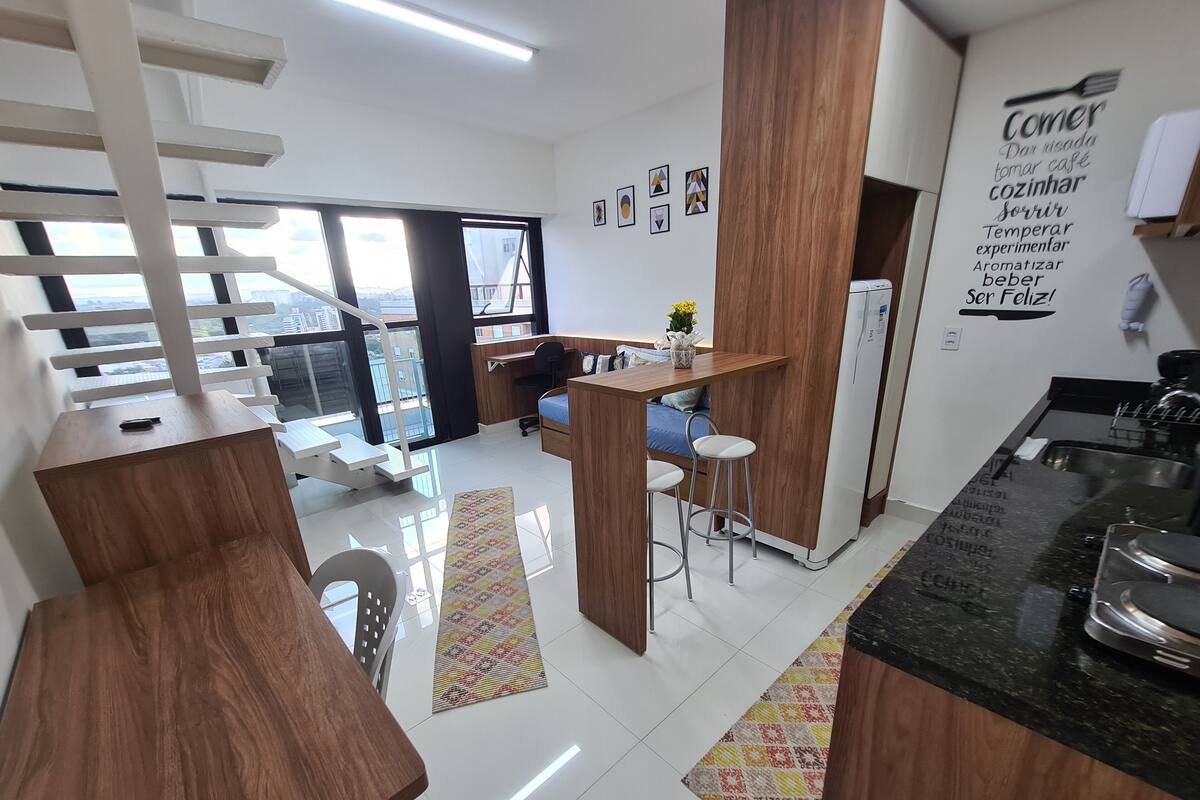 Une cuisine moderne avec un coin repas, un réfrigérateur et une fenêtre donnant sur des immeubles.