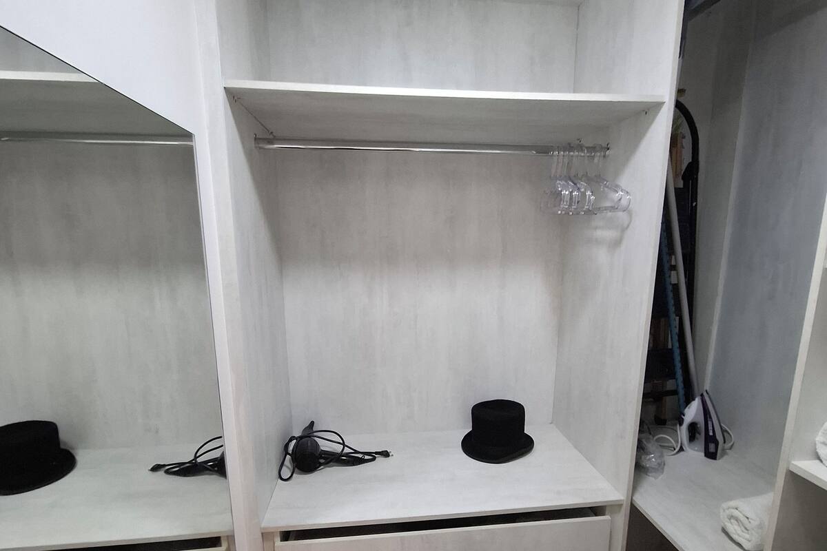 Un placard avec des étagères blanches, des tiroirs et un espace pour suspendre les vêtements.