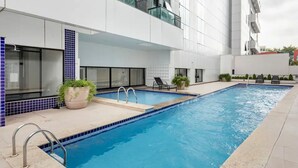 A modern building with a swimming pool, potted plants, and outdoor seating. - Edificio Selenita Loft e Duplex (Barueri)