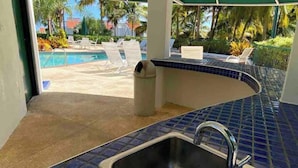 A kitchen with a sink, a tiled backsplash, and a view of an outdoor pool area. - Lovely 2 Bed room villa in luxury resort with Beach & Pool access *golf cart (Río Grande)