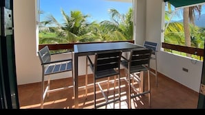 A balcony with a table and chairs, large windows with a view of palm trees and mountains. - Lovely 2 Bed room villa in luxury resort with Beach & Pool access *golf cart (Río Grande)