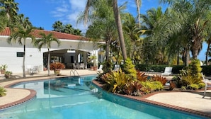 A swimming pool with a tiled edge, surrounded by palm trees and various plants. - Lovely 2 Bed room villa in luxury resort with Beach & Pool access *golf cart (Río Grande)
