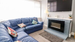 Uma sala de estar com um sofá seccional azul, uma lareira e uma TV de tela plana montada acima.