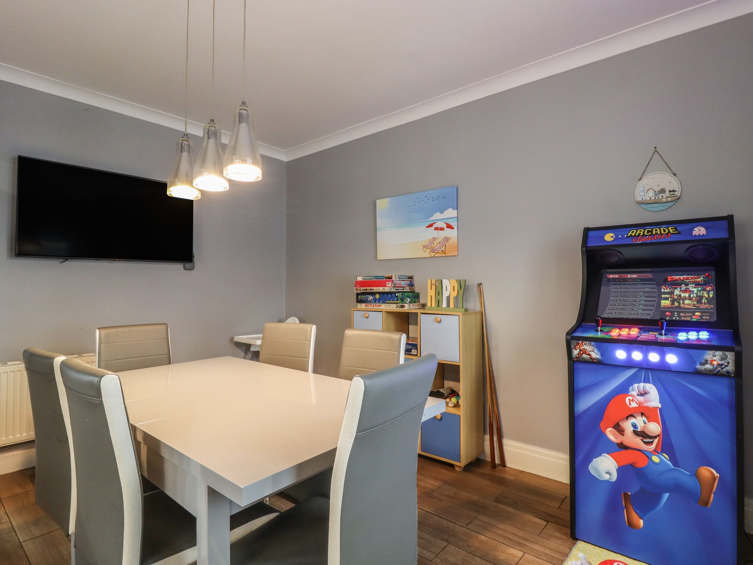 Un espace repas avec une table et des chaises, un téléviseur à écran plat et une borne d’arcade.