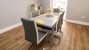 Uma sala de jantar com uma mesa posta para seis pessoas, rodeada por cadeiras, com vista para a praia pela janela.