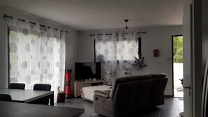 A living room with a sofa, a TV, and a dining area with a table and chairs. - Villa Contemporaine (Lattes)