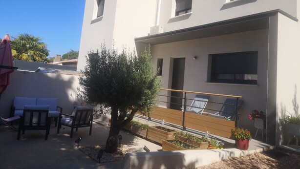 A modern two-story building with a flat roof, a balcony with a wooden floor, and a small tree in the foreground. - Villa Contemporaine (Lattes)