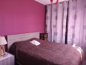 Un dormitorio con una cama, una mesita de noche, una lámpara y una ventana con cortinas.