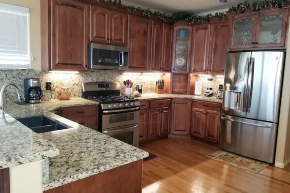 A kitchen with wooden cabinets, a stainless steel refrigerator, a microwave, a stove, and granite countertops.