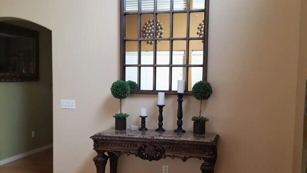 A wooden console table with a decorative mirror above it, flanked by two potted plants and three candles. - Spacious home located near Mtns & Downtown Denver! (Westminster)
