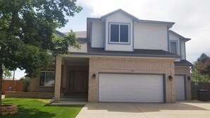A two-story house with a garage, brick facade, and a covered entryway. - Spacious home located near Mtns & Downtown Denver! (Westminster)