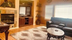 A living room with a fireplace, wooden cabinets, a black leather sofa, and a patterned rug. - Spacious home located near Mtns & Downtown Denver! (Westminster)