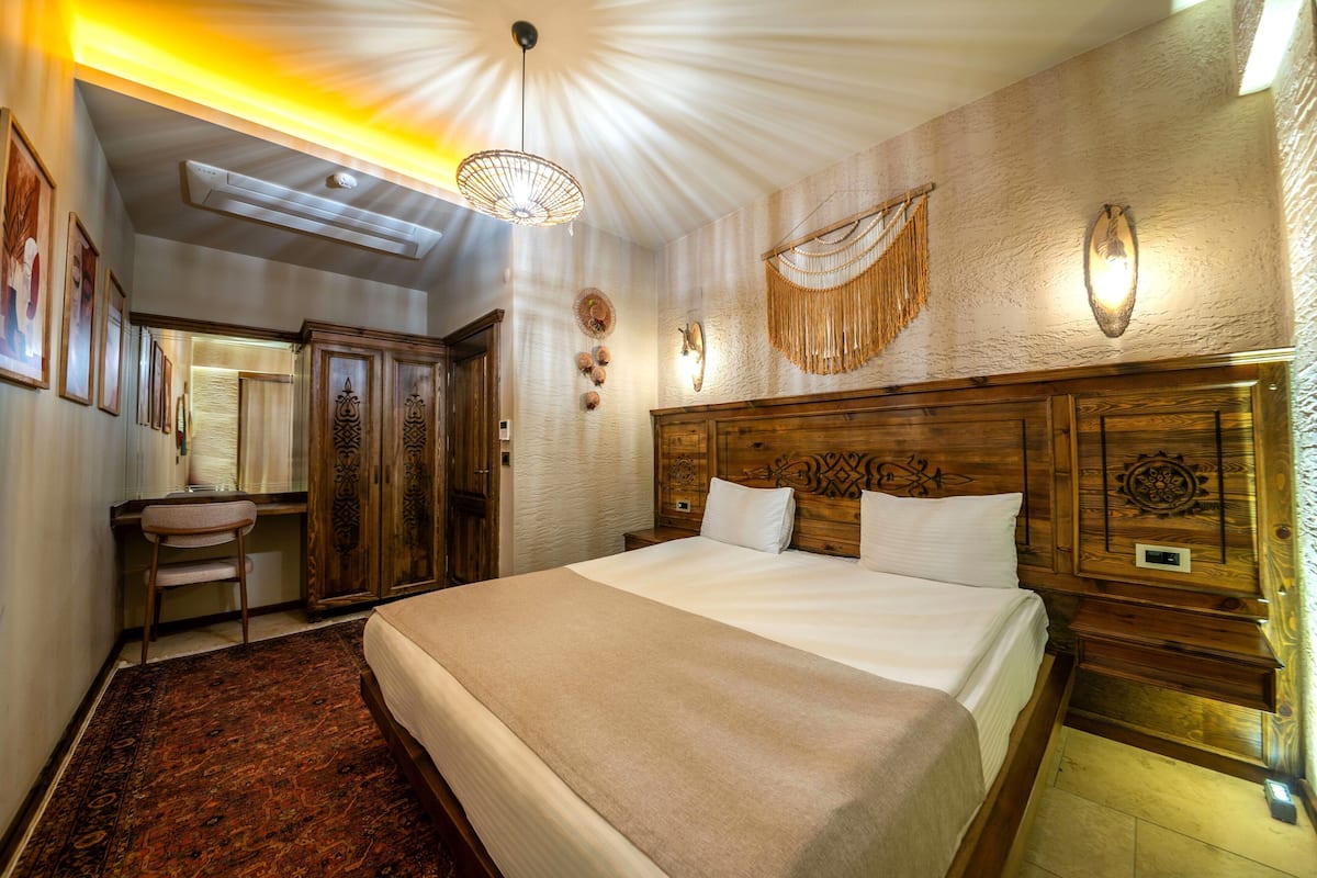 A hotel room with a large bed, wooden headboard, wall-mounted decor, and a desk with a chair.
