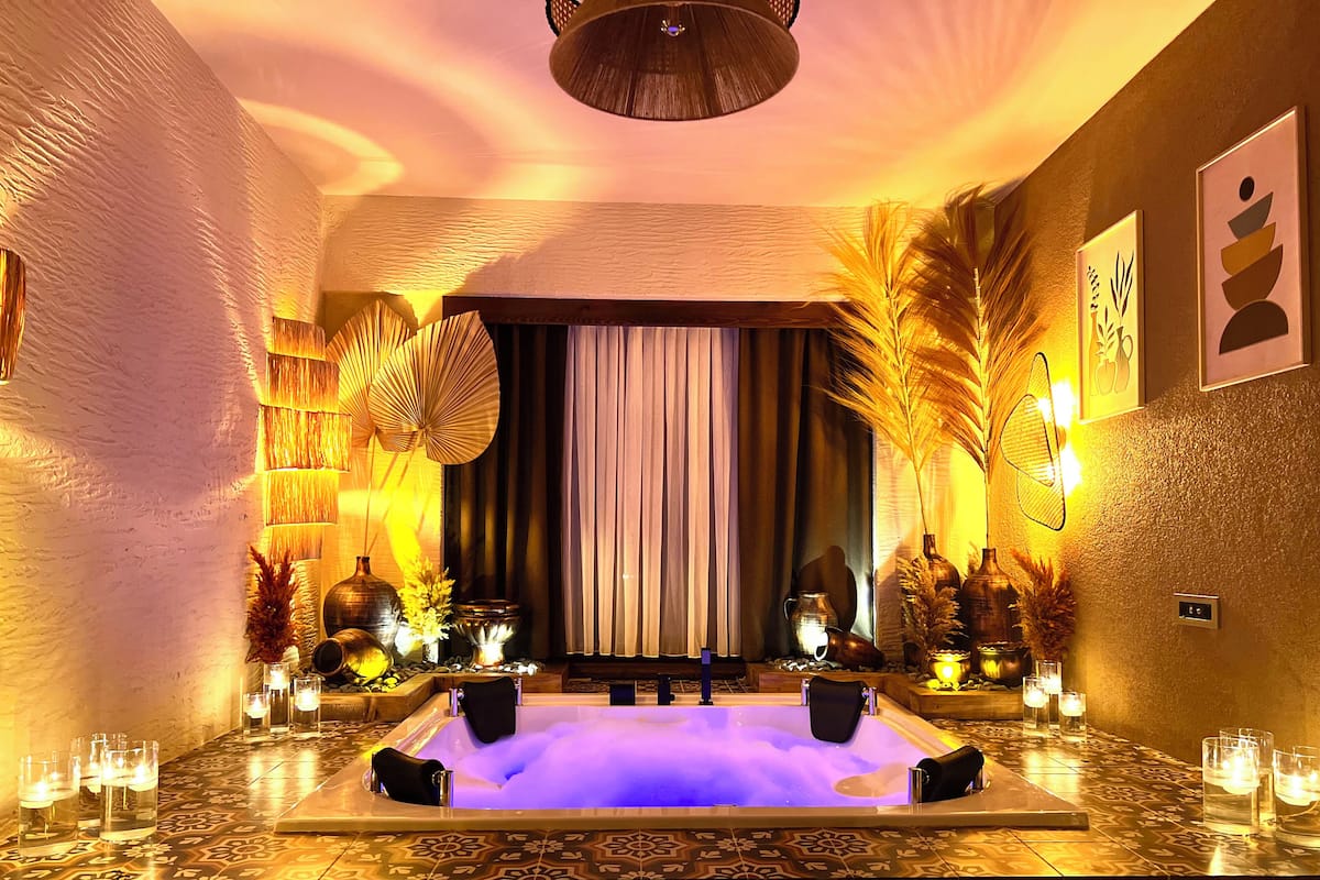 A spa room with a large bathtub, decorative plants, and candles.