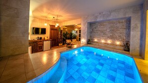 A modern indoor pool area with a stone wall, a kitchen with a bar, and a seating area.