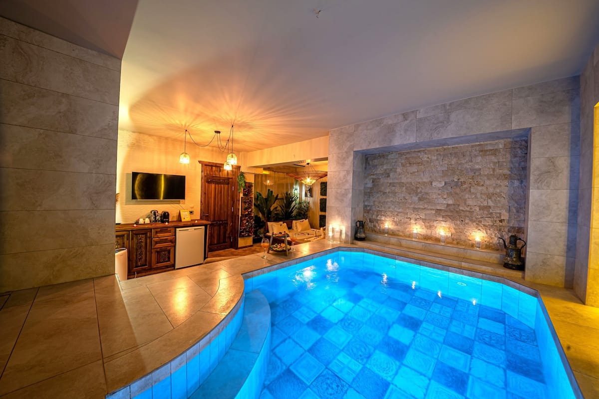 A modern indoor pool area with a stone wall, a kitchen with a bar, and a seating area.