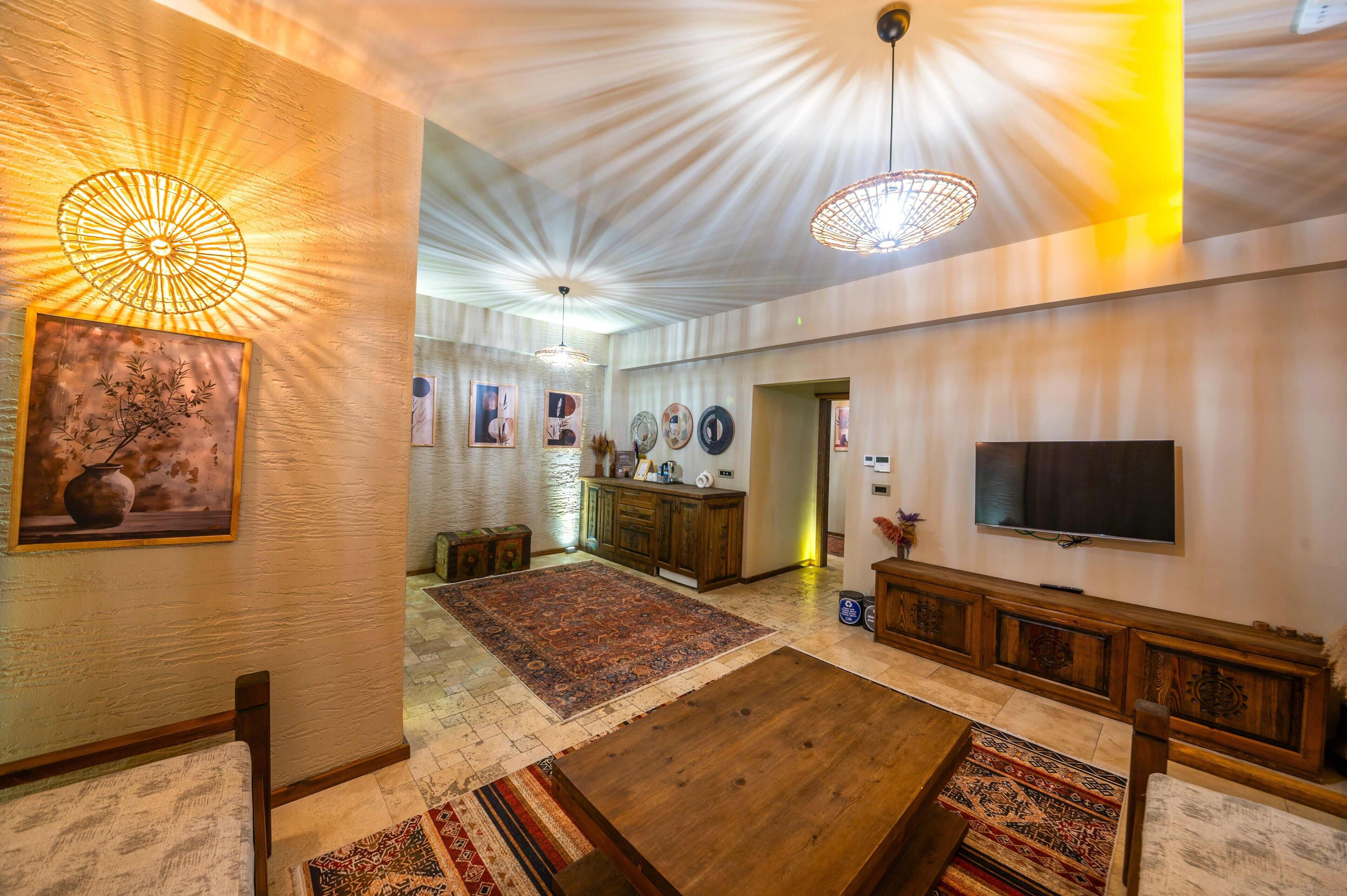 A spacious living room with a large wooden coffee table, a flat-screen TV mounted on the wall, and a traditional rug.