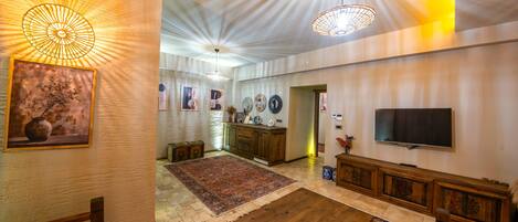 A spacious living room with a large wooden coffee table, a flat-screen TV mounted on the wall, and a traditional rug.