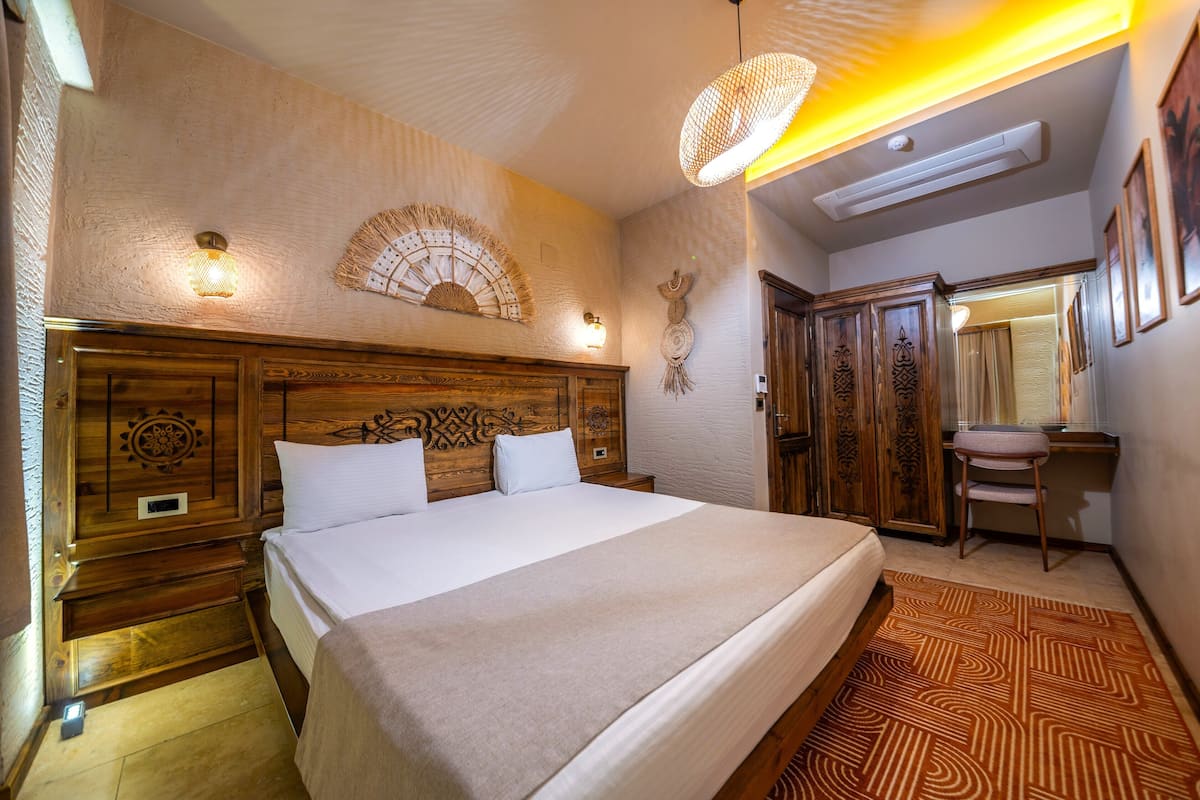 A hotel room with a large bed, wooden headboard, wall-mounted light fixtures, a desk, and a chair.