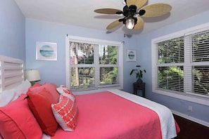 A bedroom with a bed, a ceiling fan, and two windows with blinds.