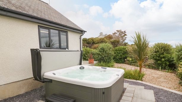 A hot tub in a garden with a house in the background. - Bryn Meilw (Holyhead)
