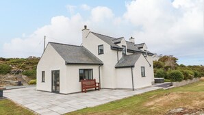 A two-story house with a tiled patio and a wooden bench. - Bryn Meilw (Holyhead)