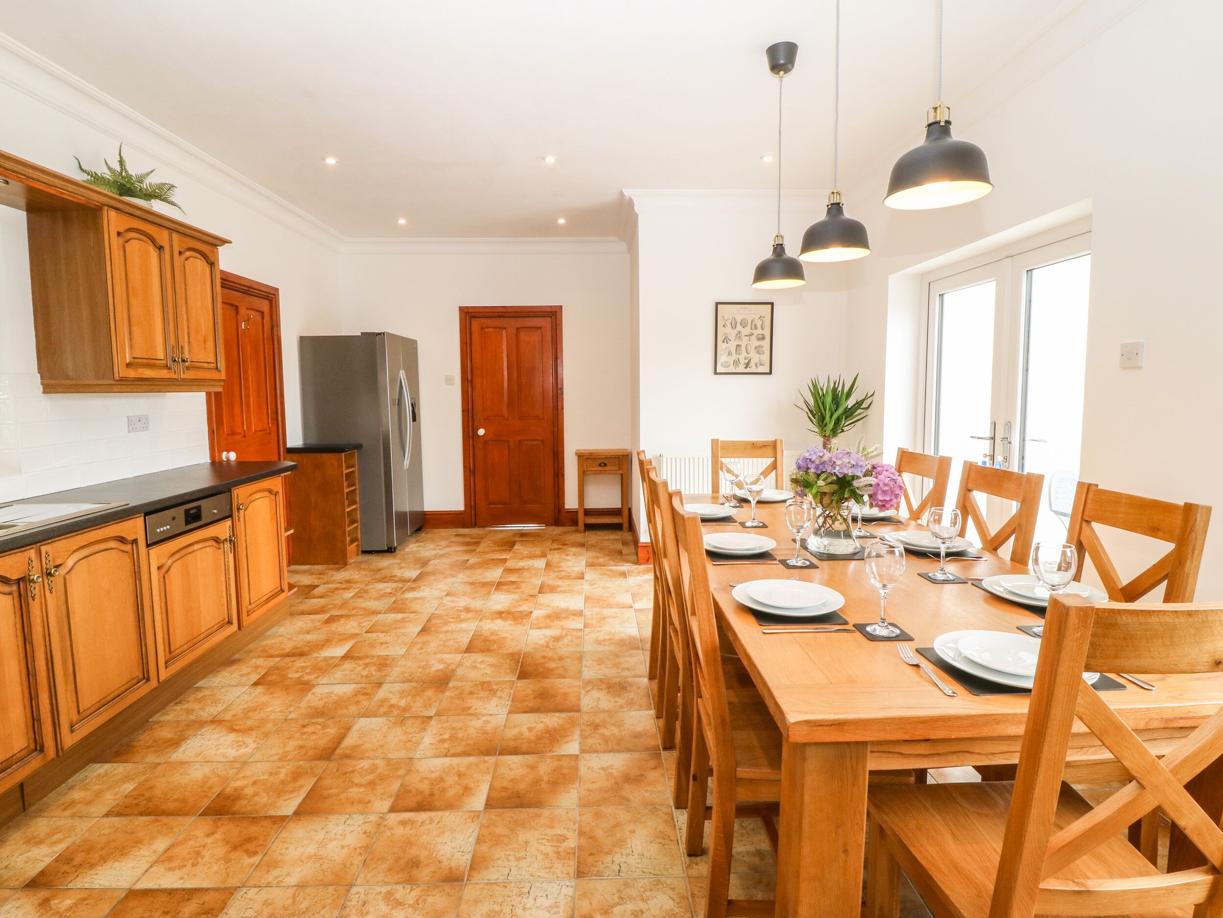 A spacious kitchen with wooden cabinets, a refrigerator, and a dining area with a wooden table set for six.