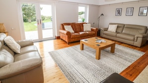 A spacious living room with a brown leather sofa, a beige sofa, and a wooden coffee table. There are two hanging wicker lamps and a floor lamp. - Bryn Meilw (Holyhead)
