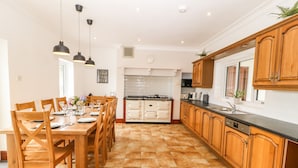 A modern kitchen with wooden cabinets, a black countertop, and a dining area with wooden chairs and a table set for four. - Bryn Meilw (Holyhead)
