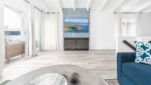 A spacious living room with a large window, a fireplace, and a view of a coastal landscape. - Remodeled & Stylish Upper-Level Home, Steps to the Sand! (Newport Beach)