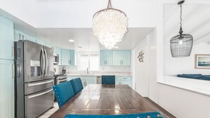 A modern kitchen with teal cabinets, stainless steel appliances, and a wooden dining table with blue upholstered chairs. - Remodeled & Stylish Upper-Level Home, Steps to the Sand! (Newport Beach)