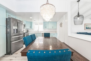 A modern kitchen with teal cabinets, stainless steel appliances, and a wooden dining table with blue upholstered chairs.