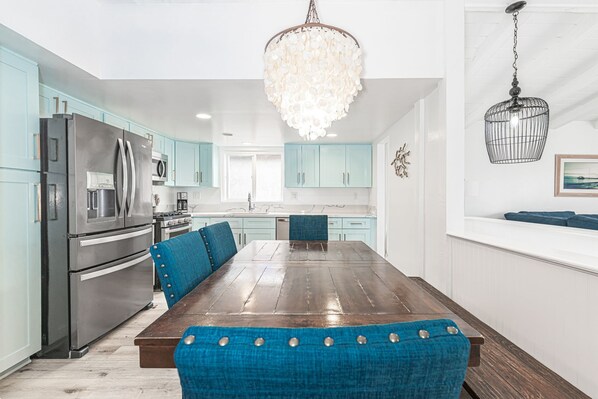 Een moderne keuken met blauwgroene kastjes, roestvrijstalen apparatuur en een houten eettafel met blauw beklede stoelen.