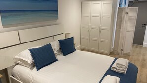 A bedroom with a bed, pillows, a painting of a beach, and a wardrobe. - Stunning Cliff Edge Apartment in Newquay (Newquay)